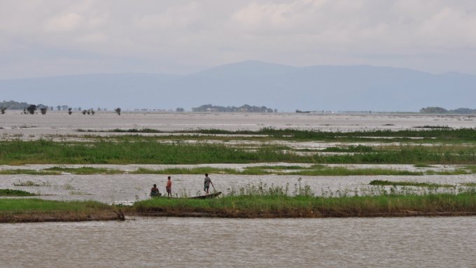 Three people on a boat look at the Ganges River with mountains in the background