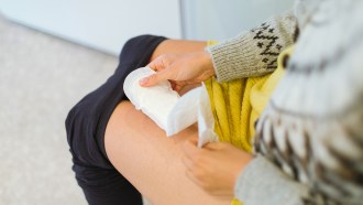 Stock photo of a person who menstruates sitting down, unpacking a period pad.