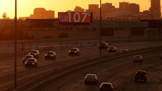 In the background, a billboard shows a temperature of 107 degrees Celsius, while cars drive eon a freeway in the foreground.